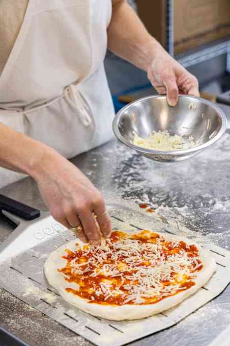 ATK Reviews member topping pizza with tomato sauce and shredded cheese before baking.